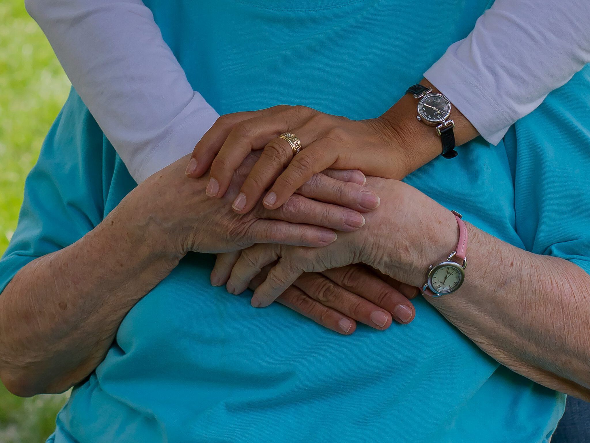 Ältere Person und Pflegeperson halten sich liebevoll die Hände auf dem Bauch